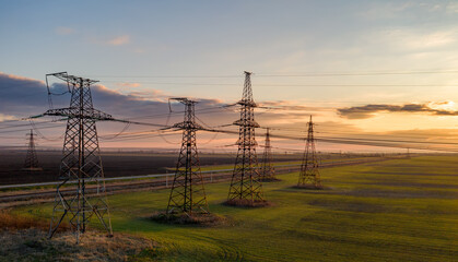high voltage lines and power pylons in a green agricultural field against a saturated sunset sky