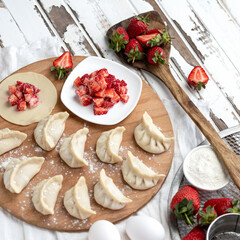 Strawberry filling and uncooked dumplings with berries on cutting board. Top view. Cooking process. Ingredients and kitchen utensils to Preparation of Convenience Food. Square format 1x1.