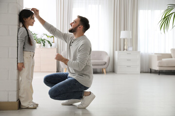 Father measuring daughter's height near white brick pillar at home, space for text