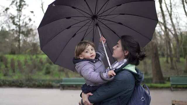 Baby toddler and mother holding umbrella outside at park during rainy drizzle day