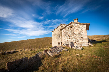 Old stone farmhouse with green and brown pastures in autumn. Lessinia Plateau (Altopiano della Lessinia), Regional Natural Park, Velo Veronese municipality, Verona Province, Veneto, Italy, Europe.