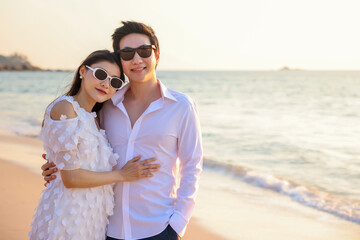 Fototapeta na wymiar Young happy Asian couple hug on the beach, romantic travel honeymoon vacation summer holidays. Asian woman and man holding hands embracing outdoors