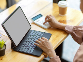 Female office worker using digital tablet and calculator on wooden table in cafe