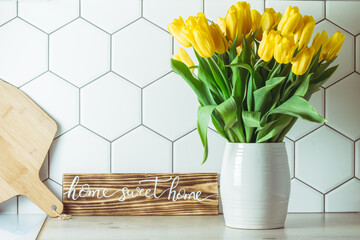 Home sweet home sign on kitchen countertop, yellow tulip bouquet in vase and cutting board on...