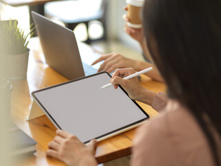 Female office worker using mock up digital tablet on wooden table with her colleague