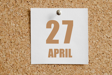 April 27. 27th day of the month, calendar date.White calendar sheet attached to brown cork board.Spring month, day of the year concept