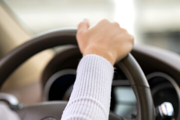 Close up view of woman holding steering wheel driving a car on city street on sunny day.
