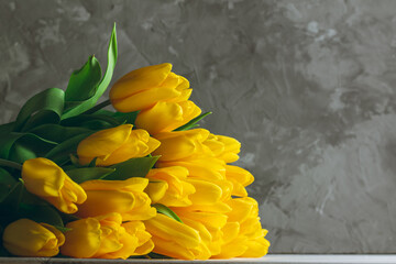 Bouquet of bright yellow tulips lying on white wooden surface on gray background. Copy space