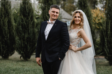 Naklejka premium beautiful newlyweds are walking in the park. wedding couple in nature. portrait of the bride and groom. wedding day of a couple in love. thuja on the background of young people.