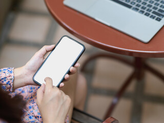 Female using smartphone include clipping path while working with laptop on round table in cafe