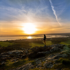 woman with her back on the mountain watching the sunset and the Dublin bay in the background