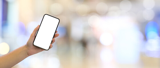 Female hand holding blank screen mock up smartphone with blurred bokeh mall background