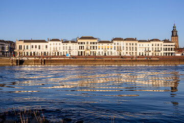 Fototapeta na wymiar Cityscape countenance of historic Hanseatic Zutphen, The Netherlands, reflecting in the river IJssel seen from the opposite shore at sunset against a clear blue sky
