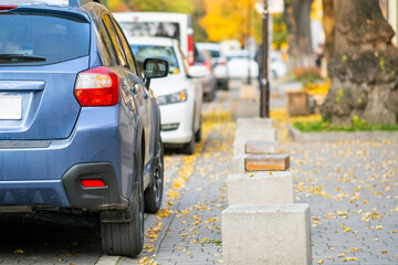 Cars parked in a row on a city street side on bright autumn day.