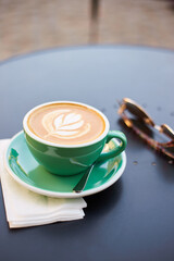 A beautiful green cup of cappuccino with trendy latte art in the table. Street coffee shop. Drinking coffee at street