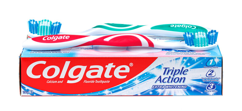 Moscow, Russia - March 27, 2021: Two colored Colgate toothbrushes on cardboard packaging of Colgate Triple Action Extra Whitening toothpaste with calcium and fluoride isolated on white background