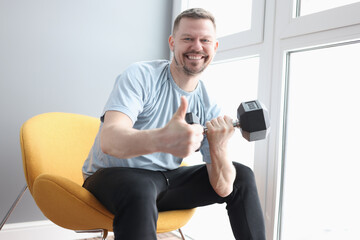 Smiling man holding a dumbbell and showing thumbs up gesture