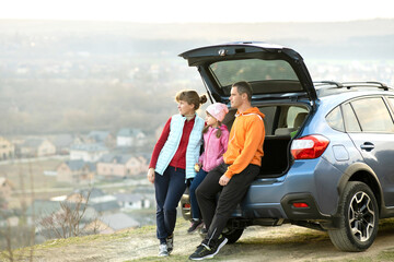 Naklejka premium Side view of happy family standing near car with open trunk and looking on nature. Concept of weekend with family on fresh air.