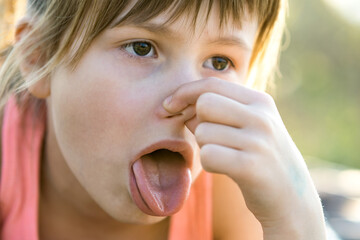 Close up of portrait beautiful child girl pinching nose and showing tongue.