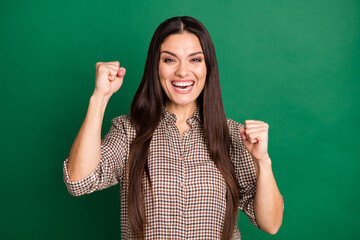 Photo of cheerful girl raise fists celebrate victory wear checkered shirt isolated green color background