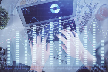 Double exposure of man's hands typing over laptop keyboard and forex chart hologram drawing. Top view. Financial markets concept.