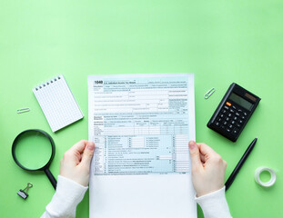 A man holds a 1040 tax form in his hands. Filling out taxation documents. Green background with copy space