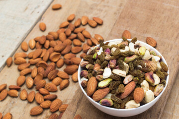 A variety of nuts are in a white bowl on the wooden background at the right of the image, top view, flat lay, top-down. selective focus.