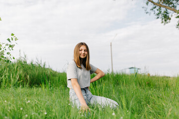teen girl in a gray T-shirt and gray jeans near a tree. Nature walk in summer, summer vacation. Lean against a tree. Quarantine