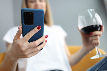Woman looks into smartphone and holds glass of wine in her hand