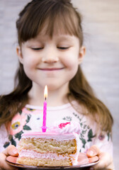 the girl holds a birthday cake with a candle in her hands and smiles