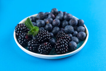 Food Photography - Blueberries and blackberries on a blue artisan plate against a blue background with mint leaves