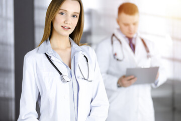 Professional beautiful woman-doctor with a stethoscope is standing with crossed arms in a sunny clinic. Young doctors at work in a hospital. Perfect medicine concept