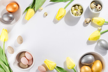 Colorful easter and quail eggs in bowl and tulips on white background with . Flat lay.