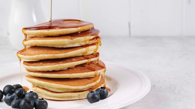 Pancake stack with blueberries and maple syrup on a white plate, copy space.