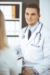 Friendly male doctor and patient woman discussing current health examination while sitting in clinic. Perfect medical service in hospital. Medicine and healthcare concept