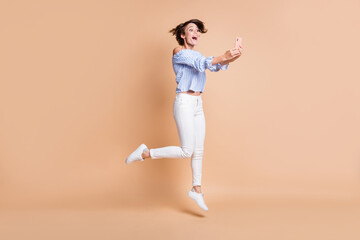 Fototapeta na wymiar Full length body size view of nice amazed cheerful girl jumping using device app 5g having fun isolated over beige pastel color background