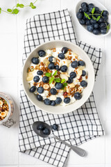 Yogurt with muesli, nuts and blueberries in a ceramic plate on the white kitchen table. Soft cream cheese with muesli and berries in a bowl top view. Healthy breakfast concept