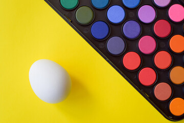 Easter painting of eggs. The set of paints lies on a yellow background. A white egg for Easter traditions.
