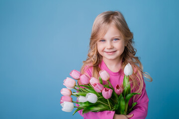 portrait of a cute little blonde girl, smiling, holding a bouquet of tulips in a pink cotton dress...