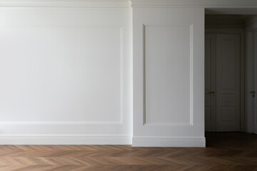 Fragment of classic interior with herringbone parquet floor and wall panels with installed moldings and skirting boards. White wall with copyspace.