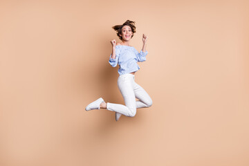 Fototapeta na wymiar Full size photo of happy victorious young woman jump up air raise fists winner isolated on pastel beige color background