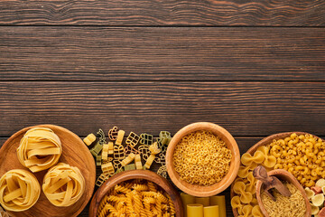 Variety of traditional italian pasta: colorful spaghetti, tagliatelle, farfalle, penne, ptititm, noodle, fusilli, cannelloni on an old wooden background. Top view with copy space.