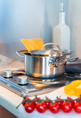 Italian spaghetti in a pan on an stove. Vegetables on the kitchen table.