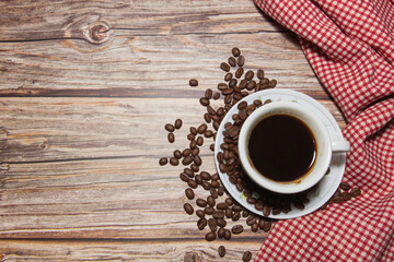 hot coffee cups and coffee beans with red patterned fabric on a wooden background.
