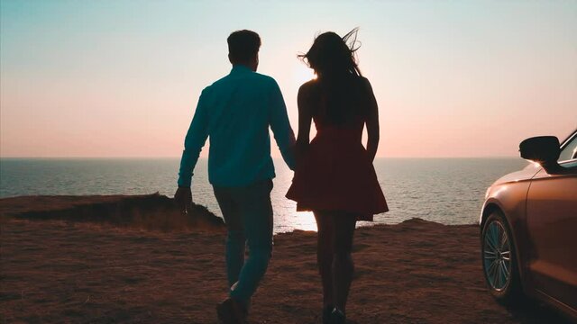 The man and woman walking near the car on the seascape background. slow motion