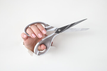 Female hand holds metal scissors in hole made of white paper