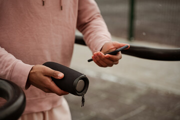 cropped view of african american sportsman holding smartphone and portable music speaker on blurred...
