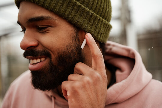Smiling, bearded African American man adjusting earphone while listening music outdoors