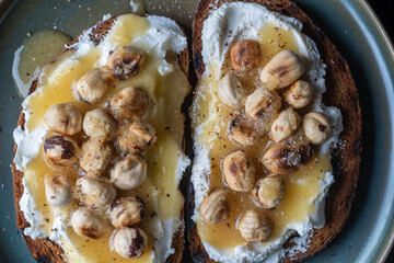 Two bread toast with cream cheese, roasted hazelnuts, honey, pepper and salt, close up, top view