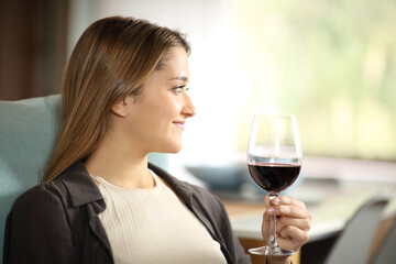 Happy woman looking away drinking wine at home